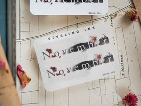 Seasonal "November" month sticker featuring rustic typography and delicate accents of dried leaves and pale pink floral illustrations for autumn journaling.