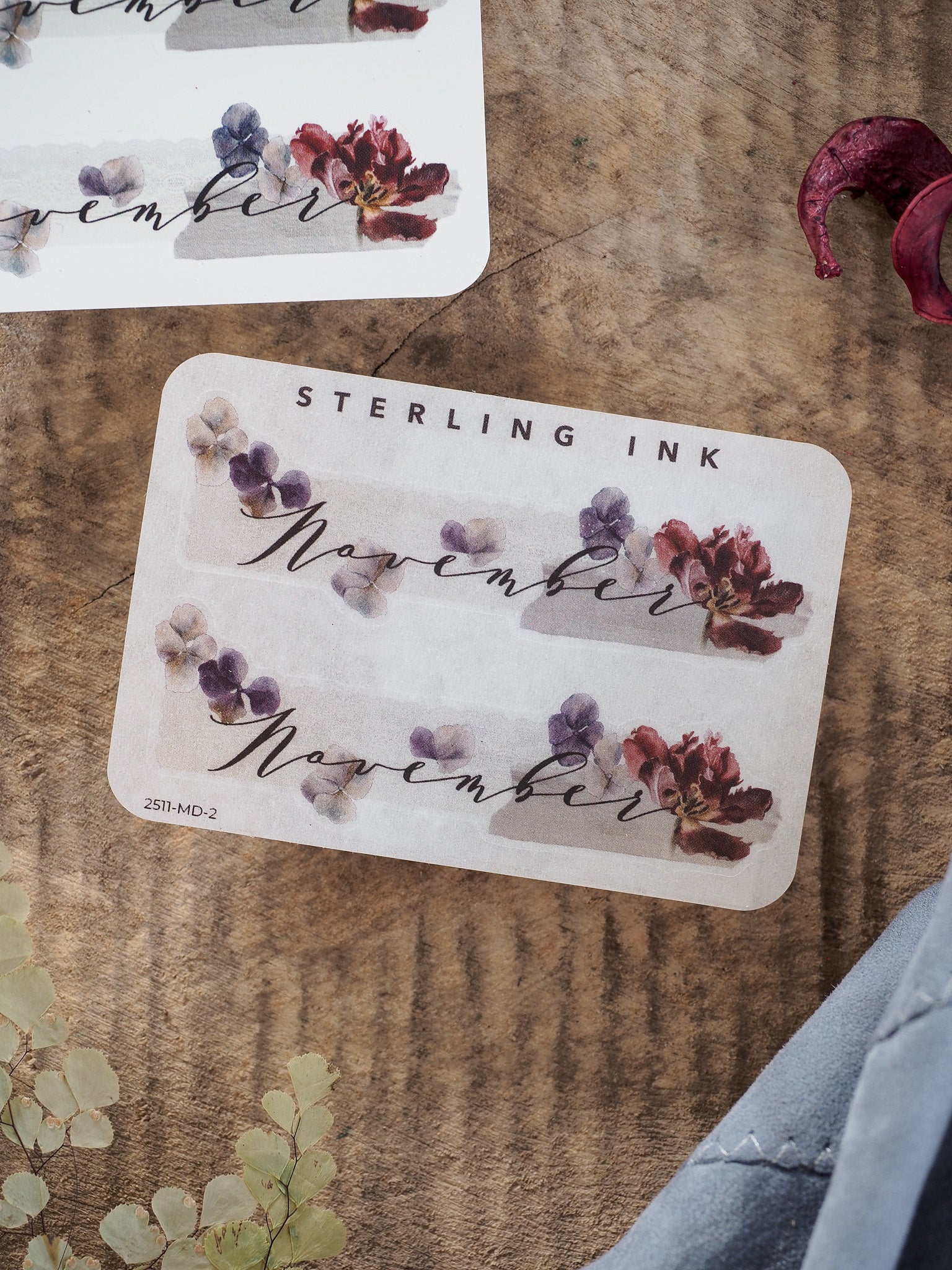 Elegant November month sticker featuring the scripted name and surrounded by delicate watercolor clusters of red and purple fall blooms.