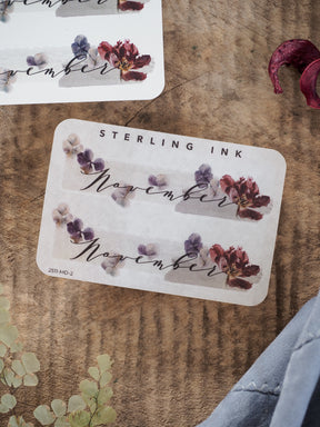 Elegant November month sticker featuring the scripted name and surrounded by delicate watercolor clusters of red and purple fall blooms.