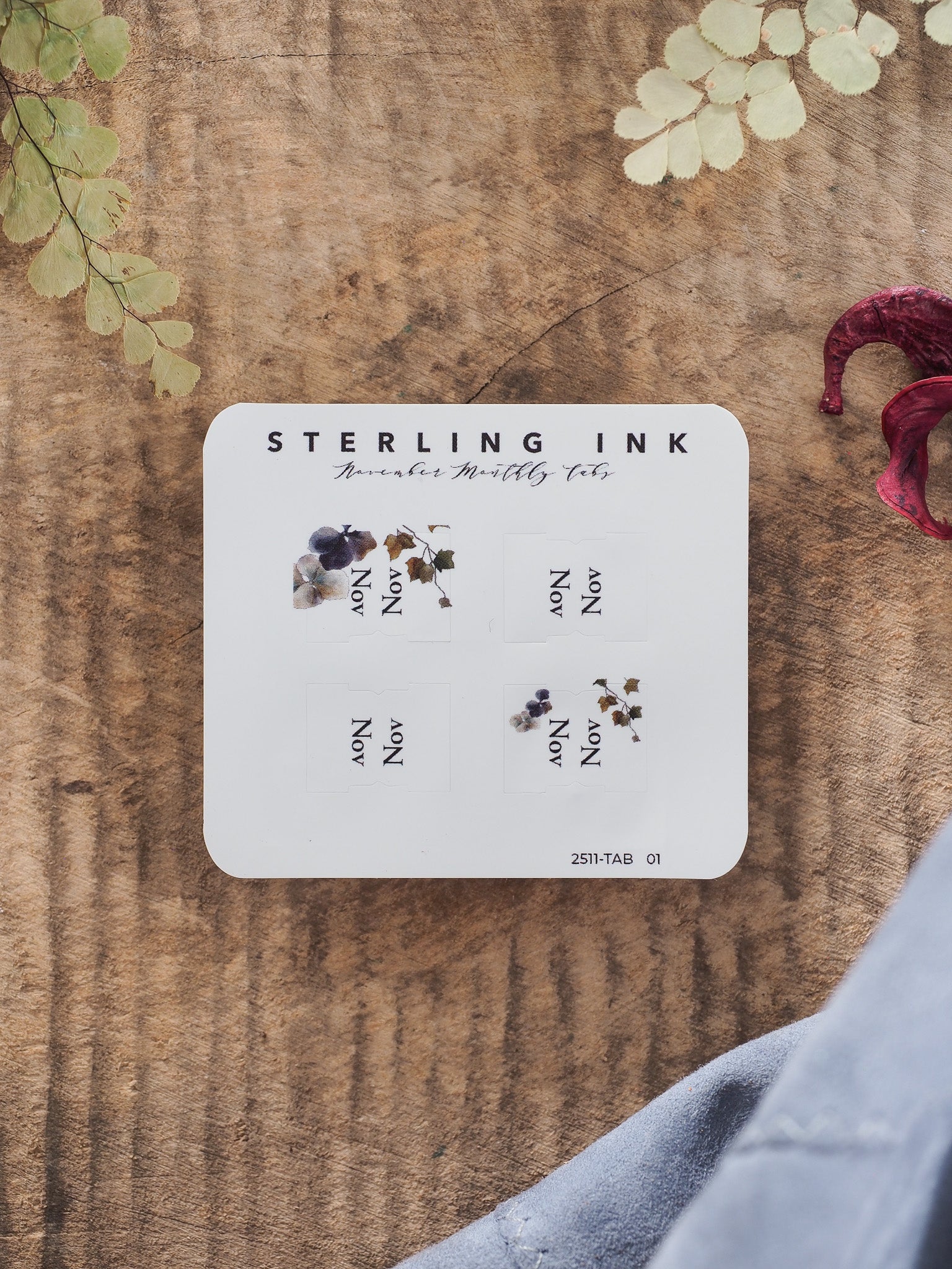White stationery card displaying four small, themed monthly tabs decorated with delicate botanical wreaths, leaves, and berries for November planning.