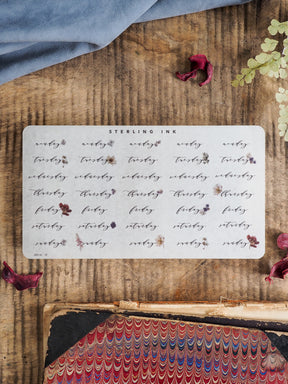 White daily planner stickers labeling weekdays, from Monday to Sunday, featuring elegant text and small decorative floral accents.