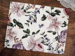 Elegant watercolor botanical print featuring soft mauve lilies, lush green foliage, and delicate blue woodland accents on white vellum.