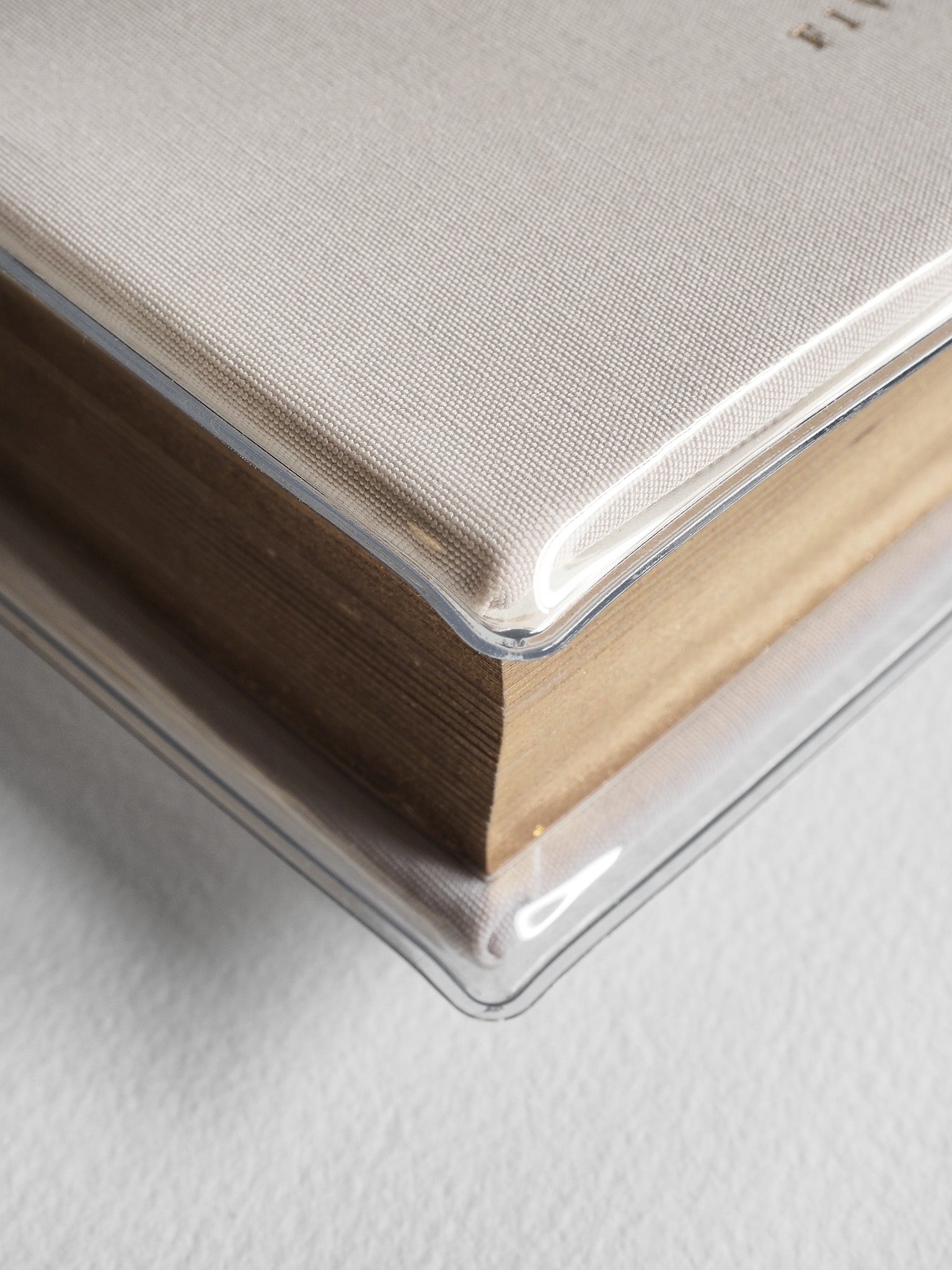 Minimalist hardcover planner featuring a textured, light taupe front cover and a clear protective sleeve over the visible stacked tan pages.