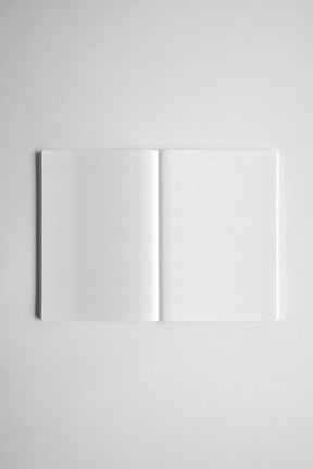 An open notebook with white graph-grid pages, photographed from above on a light gray background.