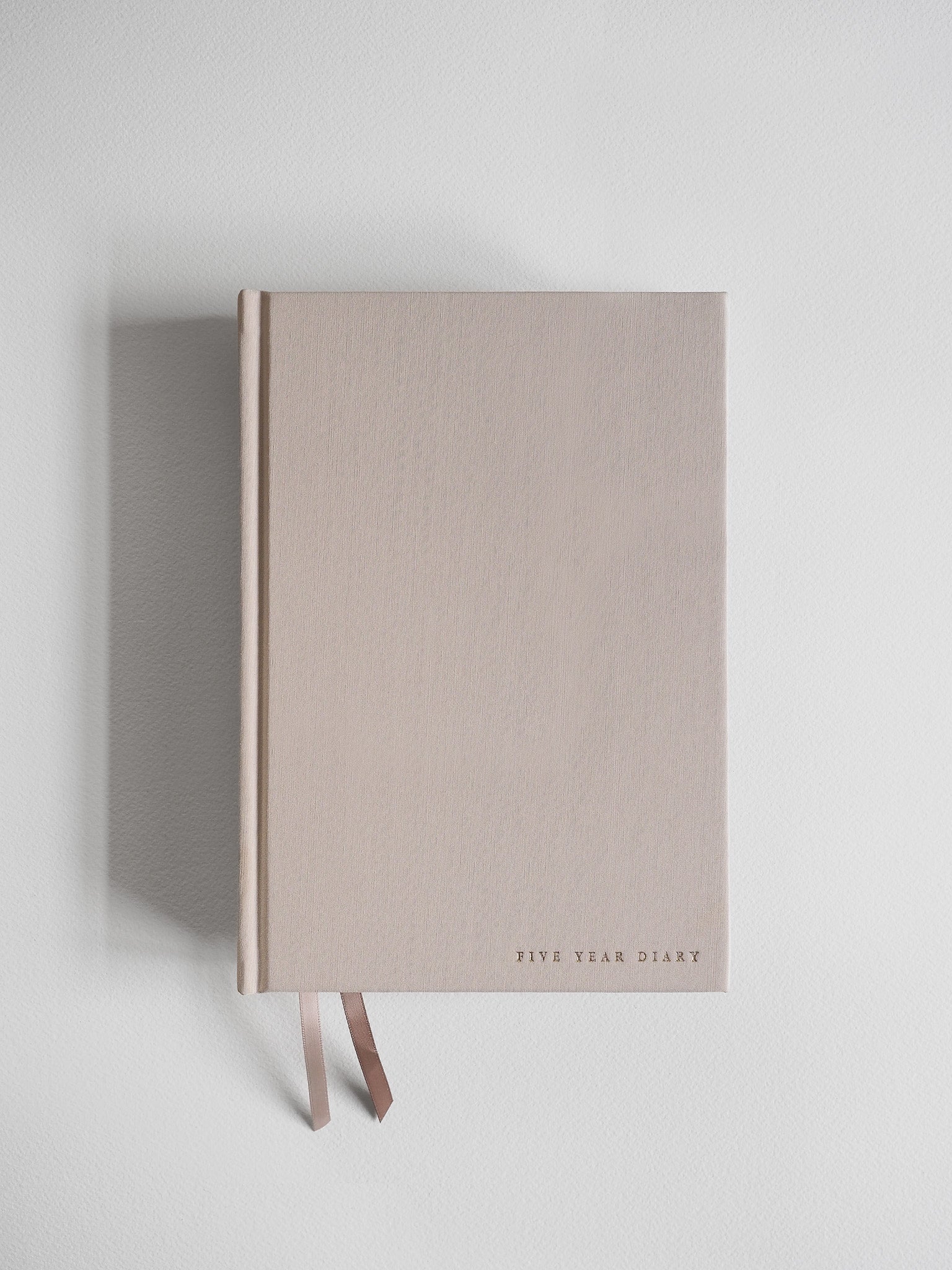 Minimalist A5 hardcover undated planner in pale beige, featuring centered typography "Five Year Diary" and accented by two delicate attached ribbons.