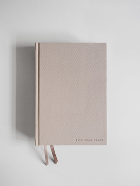 Minimalist A5 hardcover undated planner in pale beige, featuring centered typography "Five Year Diary" and accented by two delicate attached ribbons.