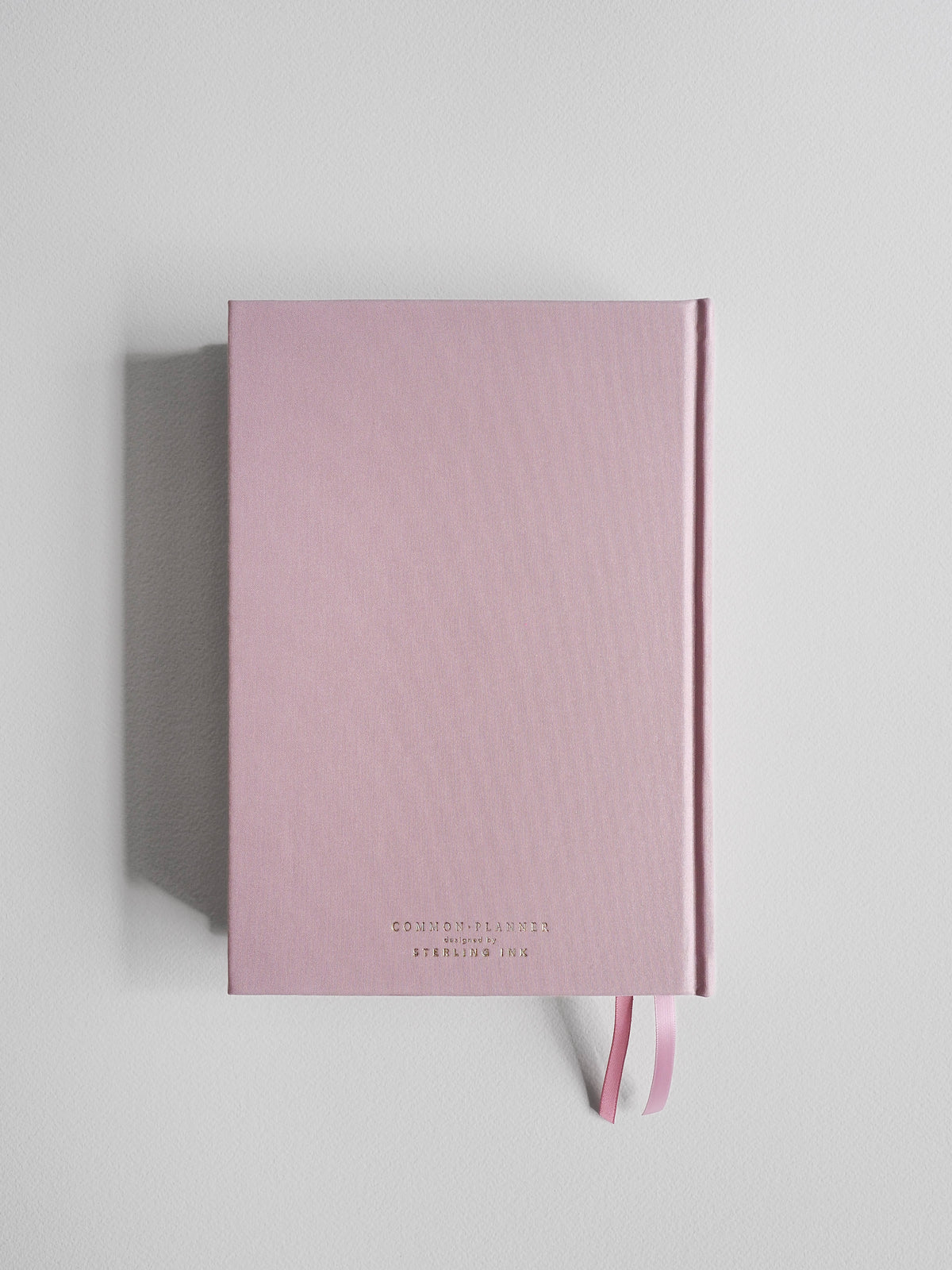 A pink hardcover notebook with a subtle diagonal ribbed texture and a matching pink ribbon bookmark, displayed on a light gray background.
#Color_Seashell