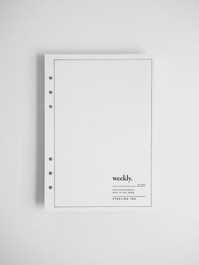 A minimalist white weekly planner or binder cover with a thin black border, five binder holes on the left, and small printed text reading 'weekly.' near the lower right, shown against a light gray background.
#Size_A5