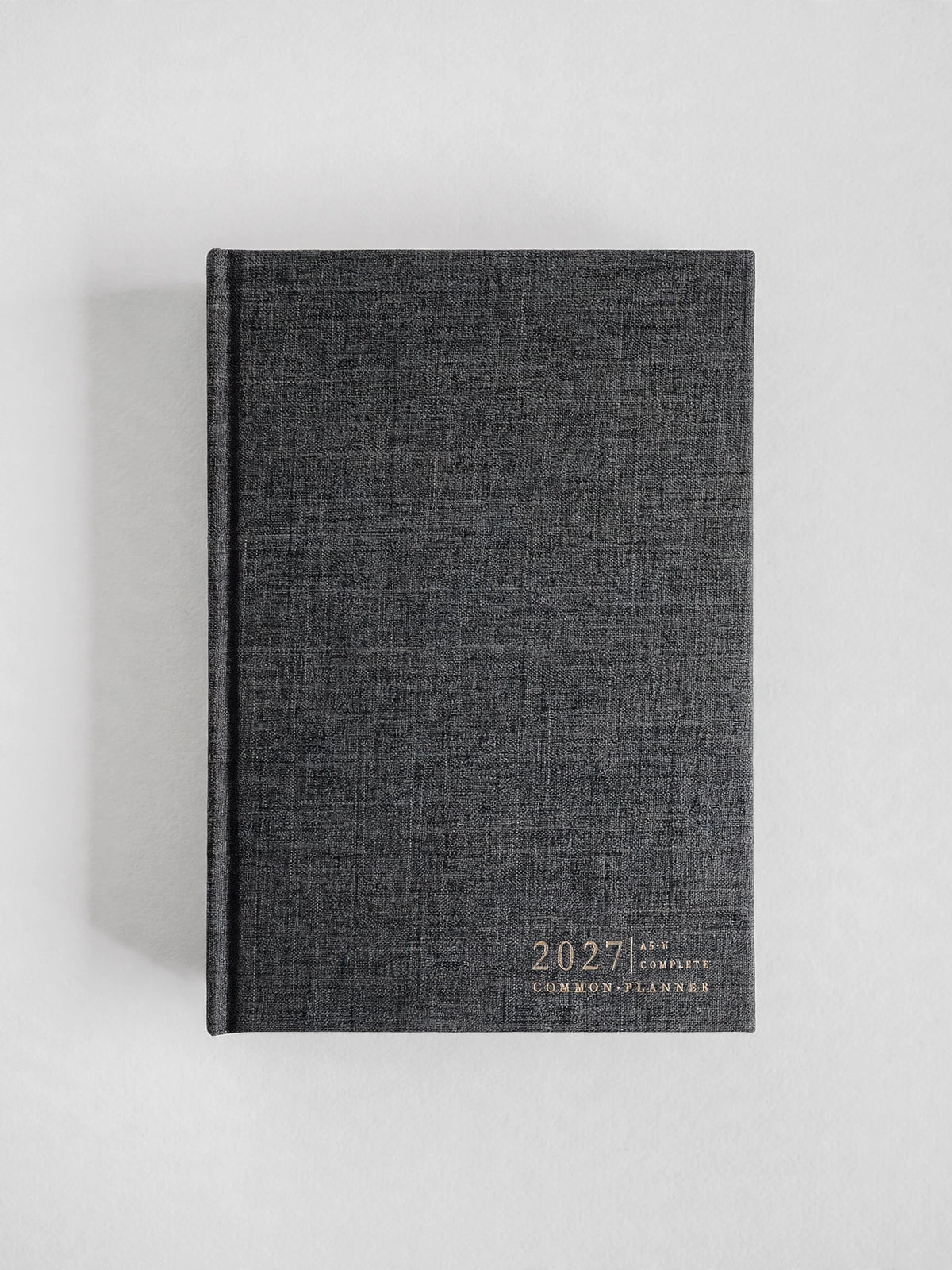 A dark gray linen-textured 2027 common planner with gold foil lettering, standing upright on a light gray background.
#Color_Charcoal