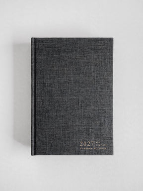 A dark gray linen-textured 2027 common planner with gold foil lettering, standing upright on a light gray background.
#Color_Charcoal