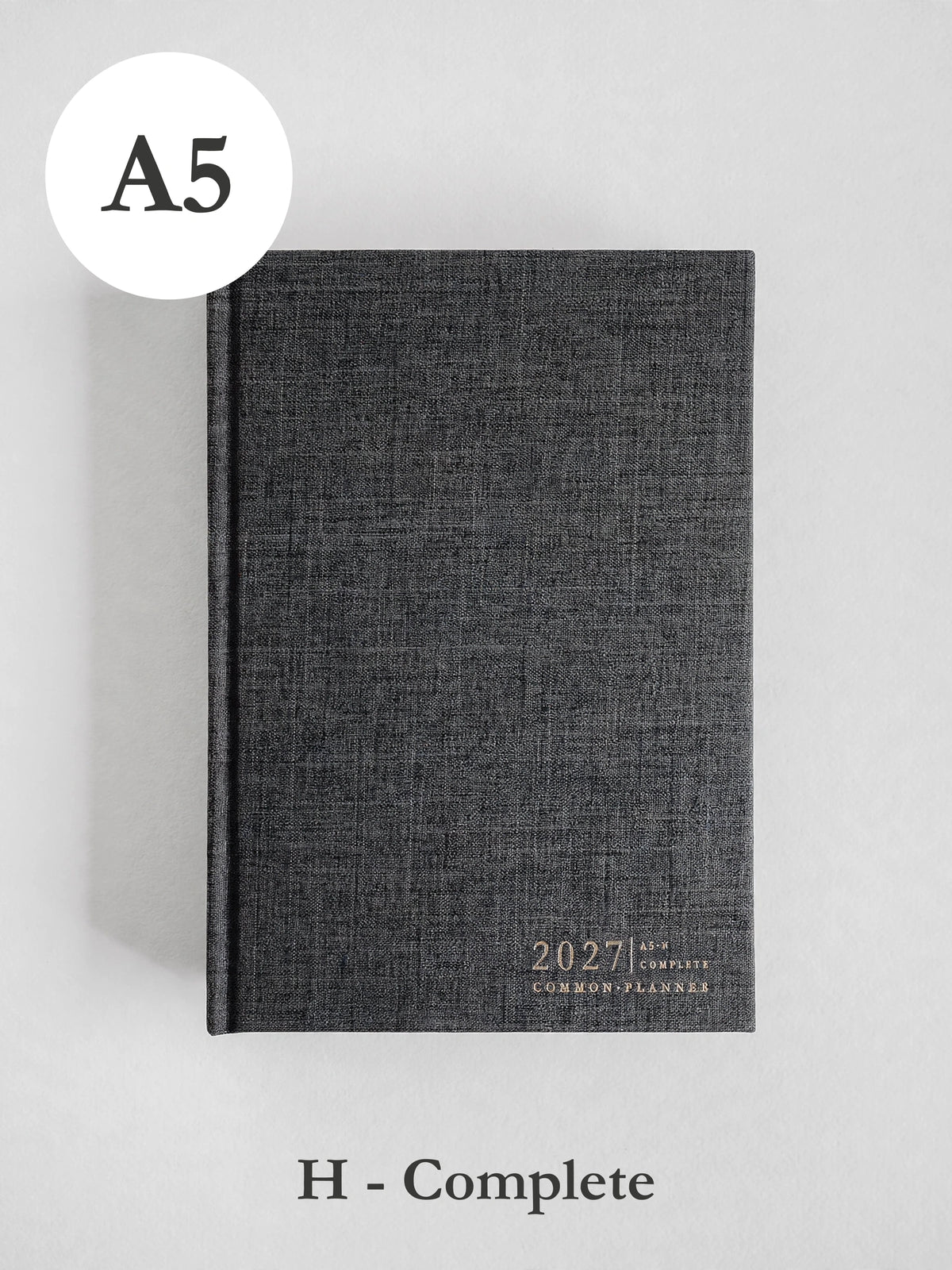 A dark gray textured hardcover planner shown closed on a light gray background, with an A5 size circle label at top left and 'H - Complete' text below.
#Color_Charcoal