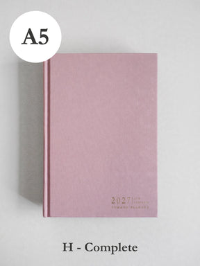 A pink hardcover planner or notebook shown closed on a light gray background, with a white circular label reading A5 at top left and text at bottom reading H - Complete.
#Color_Seashell