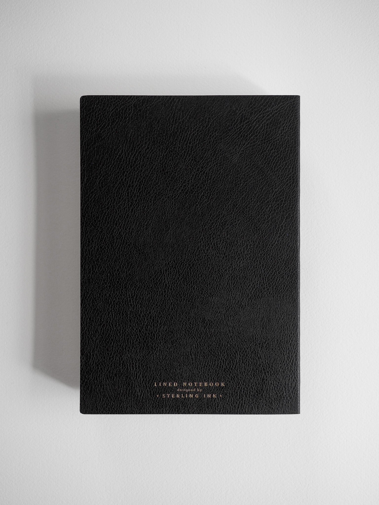 Minimalist black A5 lined notebook with a textured, deep black cover, featuring centered, embossed lettering that reads "LINED NOTEBOOK" and "STERLING INK."
