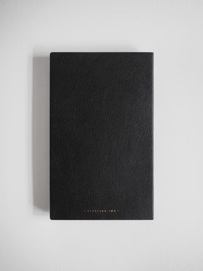 A slim A5 grid notebook with a deep black, textured cover and minimalist brand detailing, ideal for structured writing and planning.