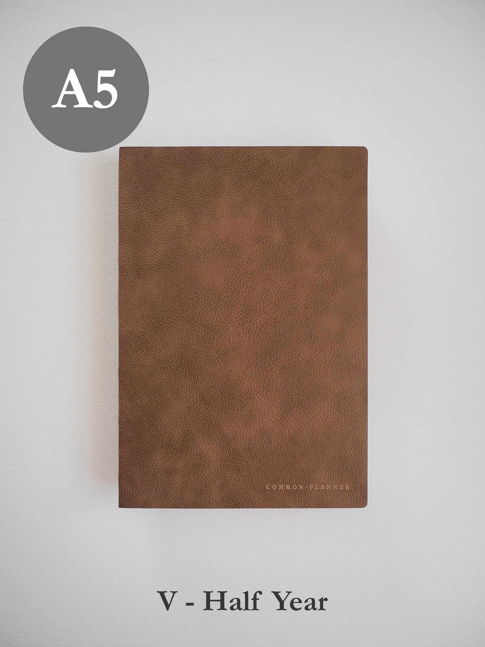 Minimalist A5 common planner cover in rich, textured cognac faux-leather, featuring subtle, elegant branding embossed near the bottom center.