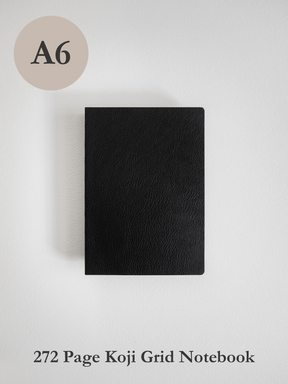 A solid black A6 notebook cover, featuring a minimalist, smooth finish, designed for a 272-page grid journal experience.