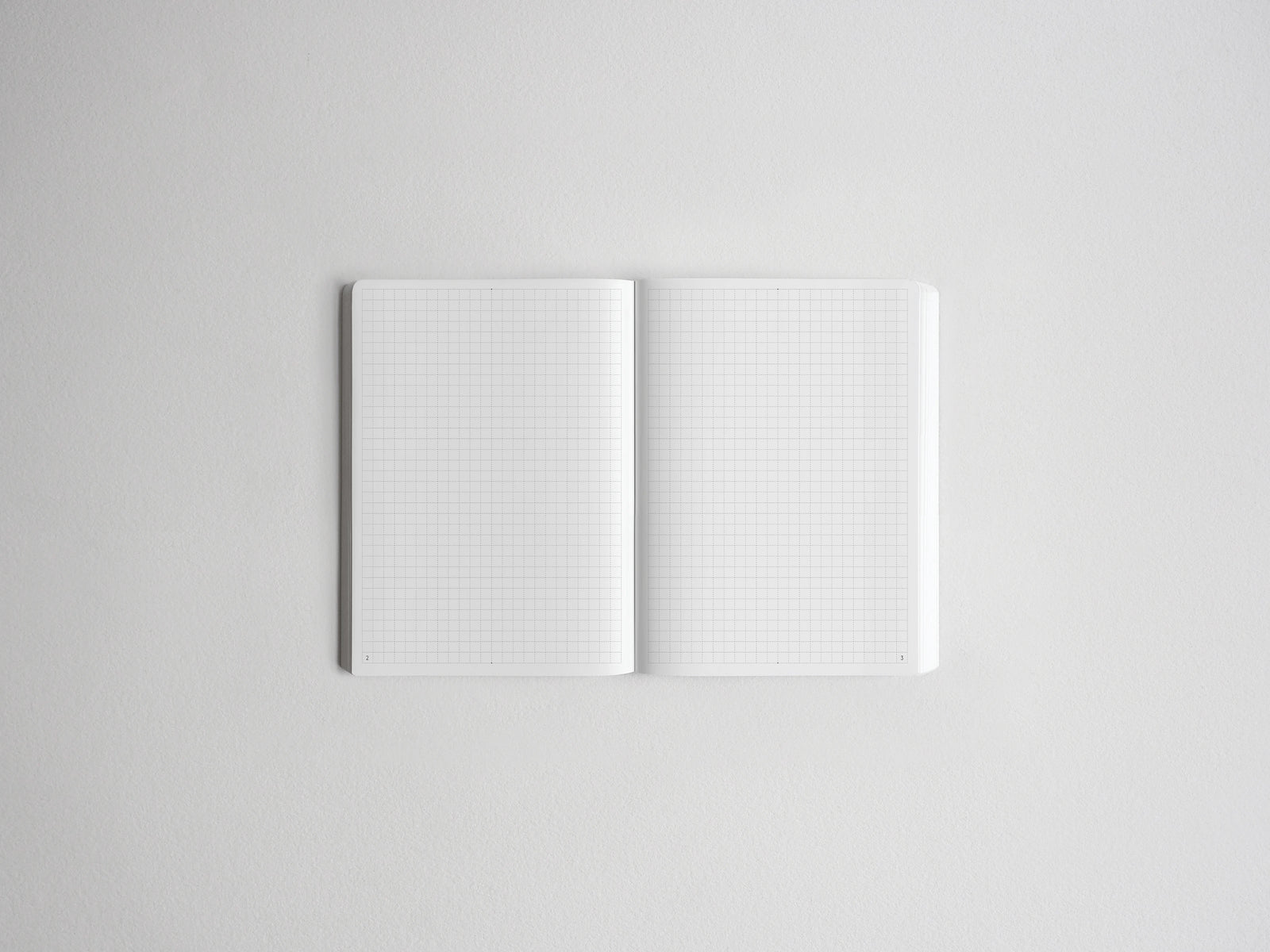An open white grid notebook with blank pages, photographed from above on a light gray background.