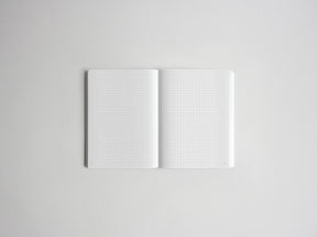 An open white grid notebook with blank pages, photographed from above on a light gray background.