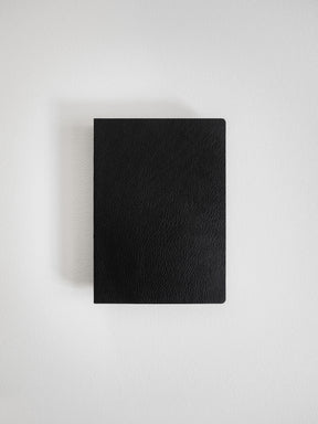 Sleek, A6-sized journal with a solid black, textured faux leather cover, ideal for grid-notebook layouts and writing notes.