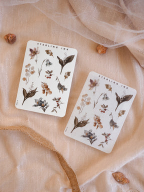 Sticker sheets featuring delicate, hand-illustrated botanical elements, showcasing dusty floral clusters and varied foliage in muted, earthy autumnal tones.