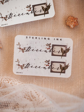 Elegant December month sticker set featuring a scripted font framed by rustic borders and accented with muted watercolor berries and dark leaves.
