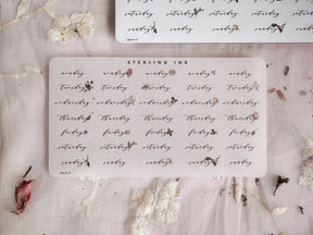 Set of cream-colored stickers featuring delicate black script lettering of "Weekday" and decorative botanical doodles for planning or journaling.
