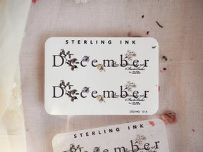 Elegant white sticker designed for December, featuring delicate botanical decals and classic black typography illustrating muted natural florals.