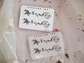Elegant white stickers featuring "December" in ornate black calligraphy, beautifully decorated with delicate script and botanical floral motifs.