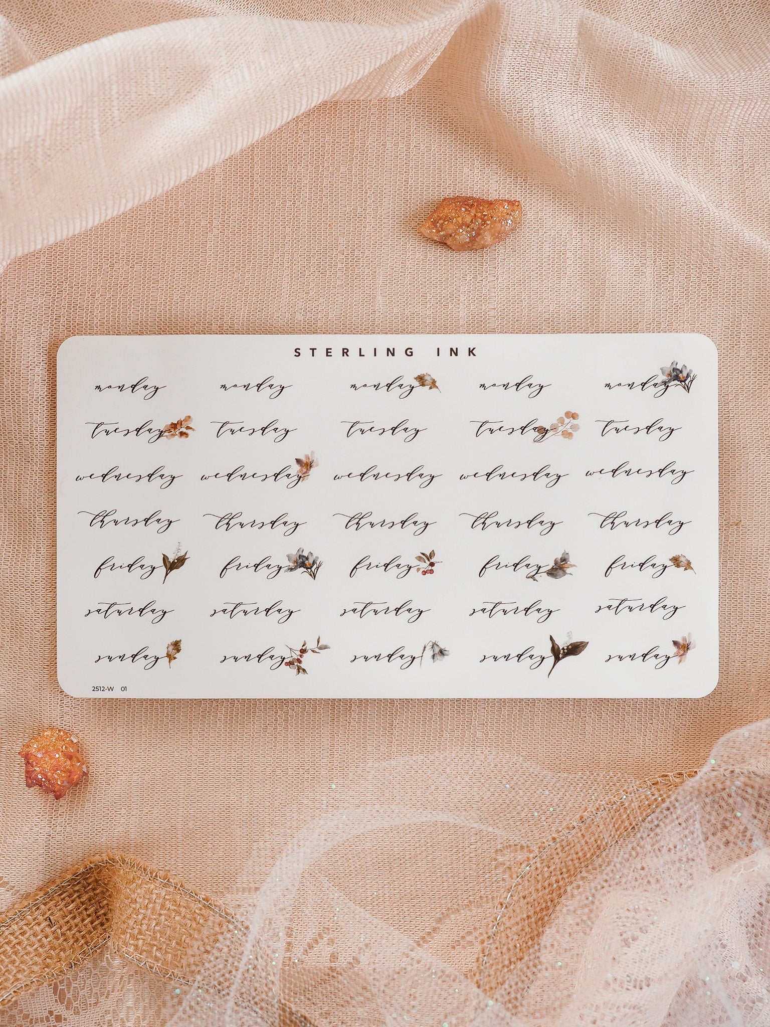 Cream-colored planner stickers marking the days of the week, featuring elegant black lettering and delicate watercolor floral accents for organizing schedules.