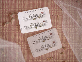 Festive "December" month planner stickers printed on cream paper, featuring rustic and delicate seasonal floral and leaf illustrations.