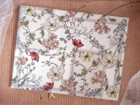 Intricate, vintage botanical print featuring delicate cream and sage florals, autumnal blooms, and flowing vine detailing against a light background.