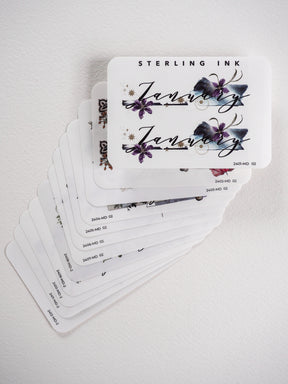 Decorative monthly sticker set featuring elegant floral illustrations, deep purple and blue watercolor blooms, and graceful script calligraphy for each month.