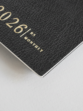 Dark grey B5 monthly booklet cover with elegant, embossed gold typography featuring the year "2026" and the word "MONTHLY."