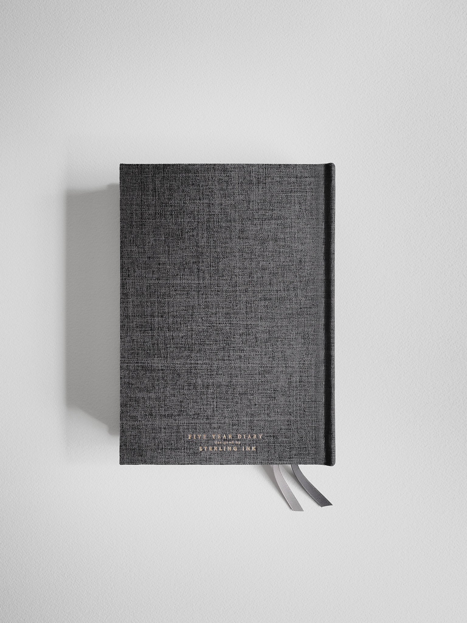 Textured dark charcoal hardcover diary featuring embossed central branding and a sophisticated linen-look finish.