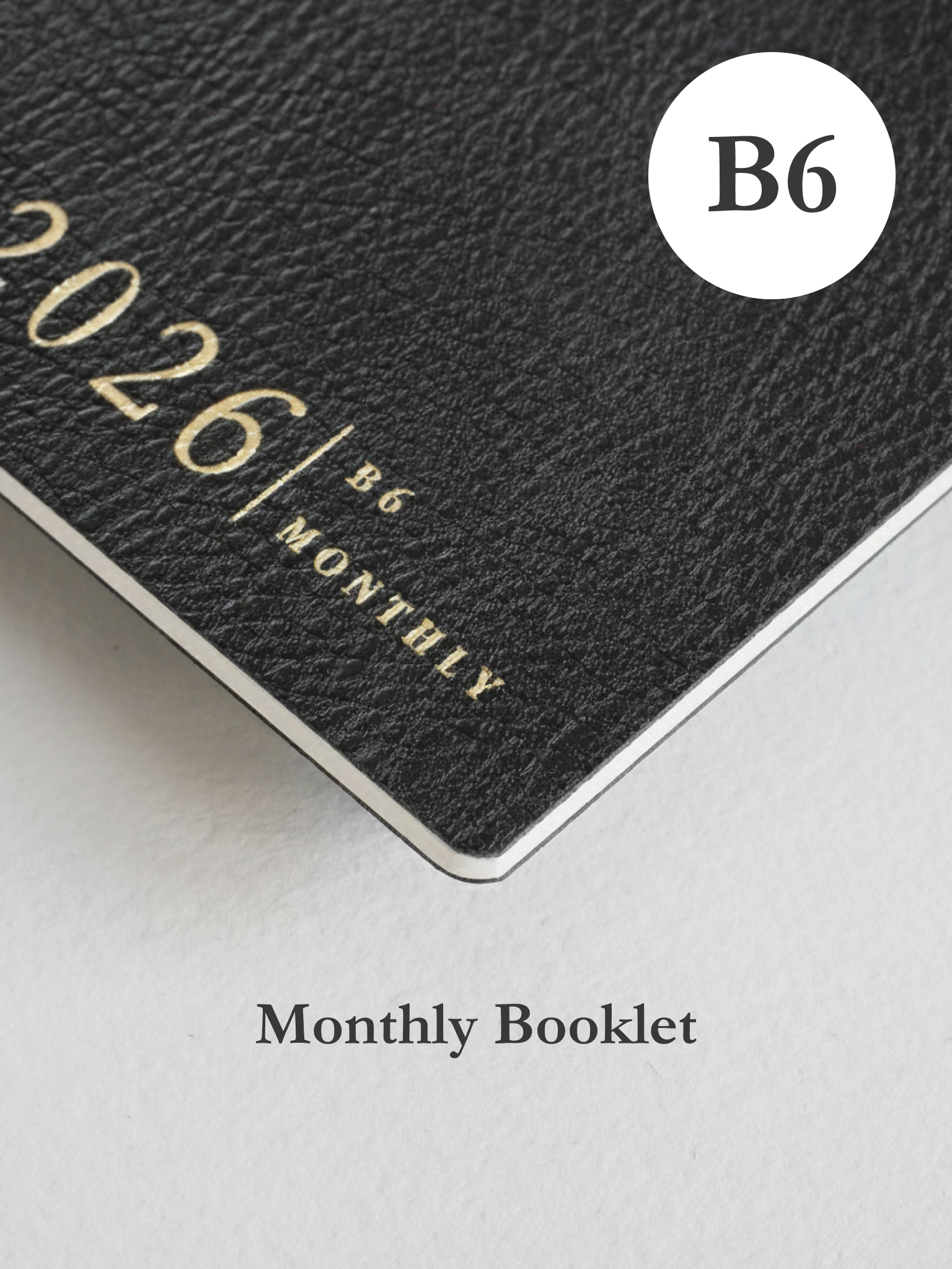 Matte black monthly planner booklet featuring bold white embossing for "2026 / B6 MONTHLY," indicating a structured calendar design.