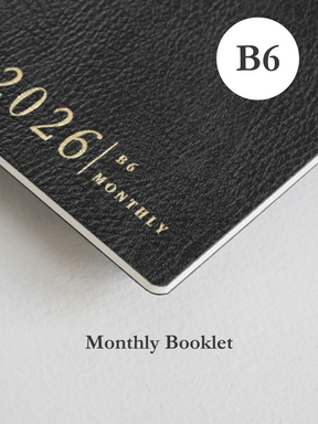Matte black monthly planner booklet featuring bold white embossing for "2026 / B6 MONTHLY," indicating a structured calendar design.