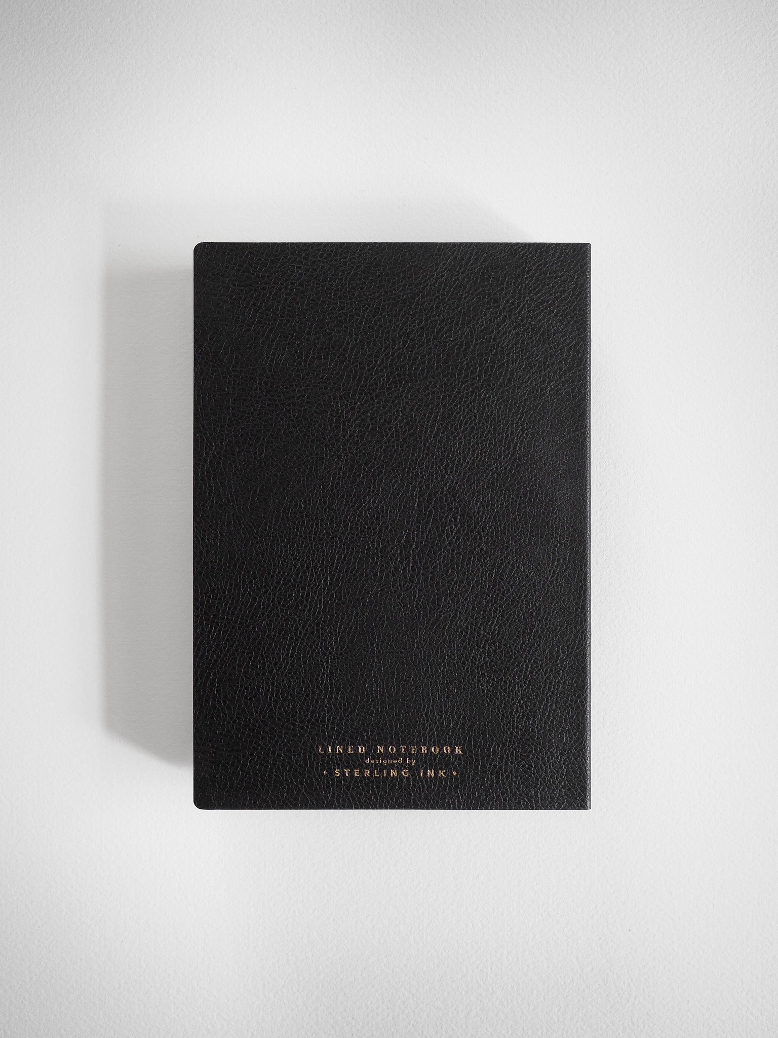 A B6-sized, matte black lined notebook featuring a textured cover and elegant gold foil branding that reads "Lined Notebook."