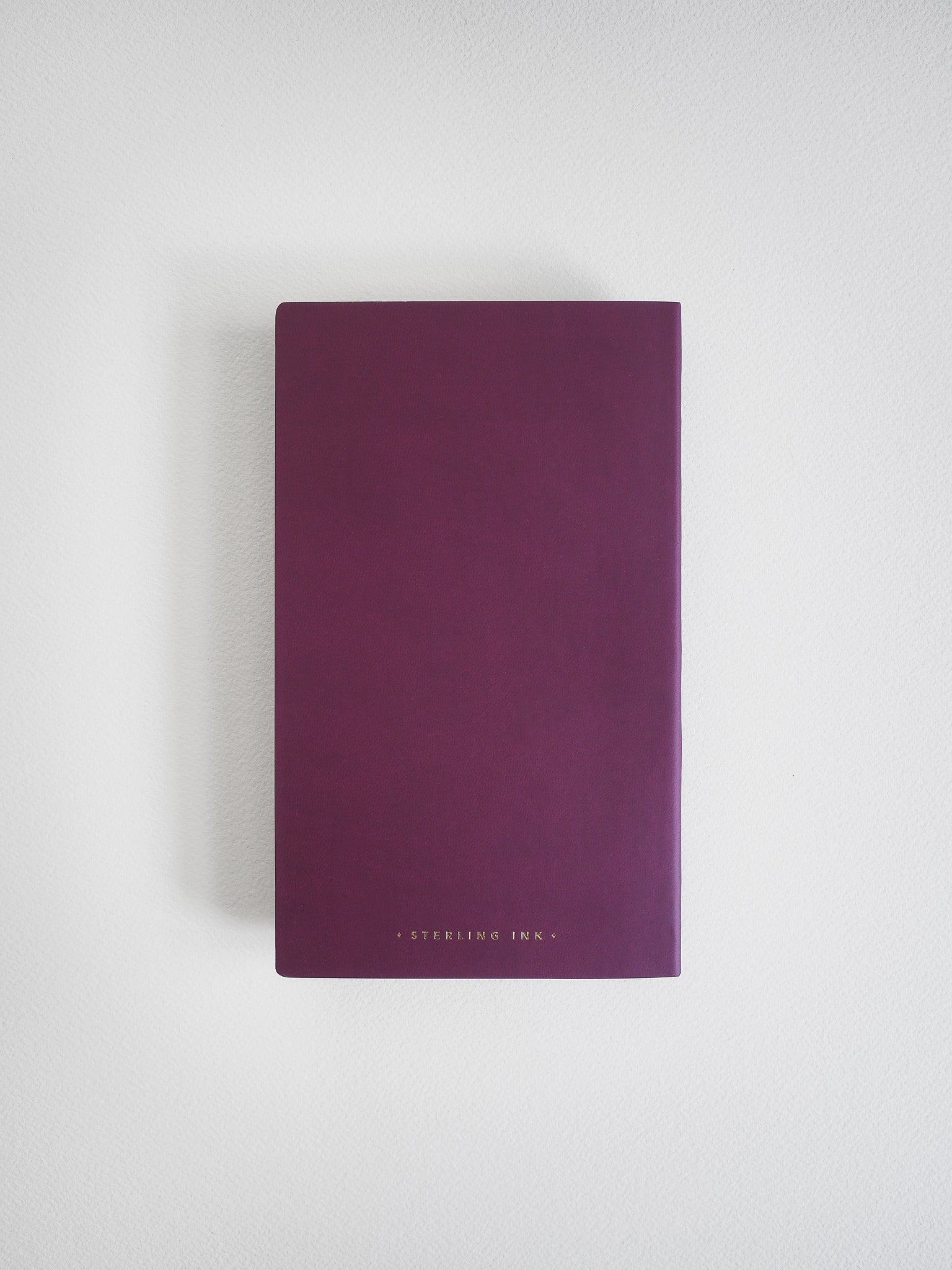 A slim B6 grid notebook with a matte, deep plum cover, featuring subtle centered black branding for "Sterling Ink."