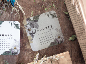 Elegant calendar grid for January 2025, framed by detailed botanical illustrations of foliage and soft white flowers.