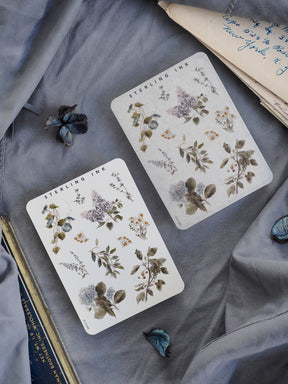 Botanical sticker sheets featuring muted, vintage watercolor depictions of seasonal floral elements, including leaves, purple blooms, and dusty greenery.