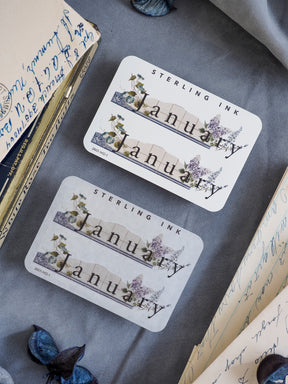 Elegant January month sticker featuring a botanical, watercolor wreath of delicate blue and green foliage around the name.