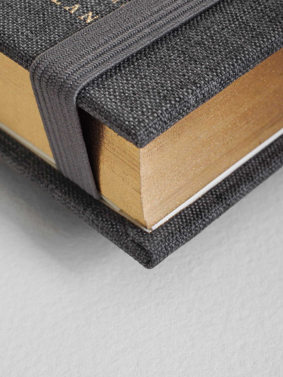Close-up of a book with textured black cover and beige pages on a light gray background
#Color_Charocal