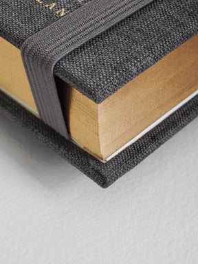 Close-up of a book with textured black cover and beige pages on a light gray background
#Color_Charocal