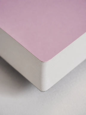 A close-up of a notebook or book corner showing a dusty pink top cover and white stacked pages, photographed on a light neutral surface.
#Color_Fairyfloss