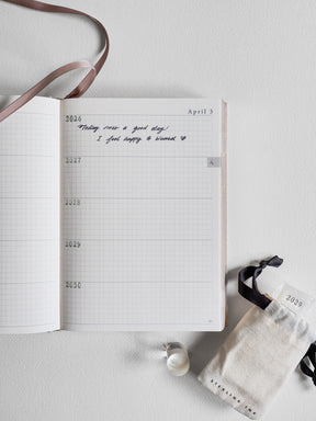 Open five-year diary planner with gridded paper, displaying structured journaling pages and dated entries for years 2026 through 2030.