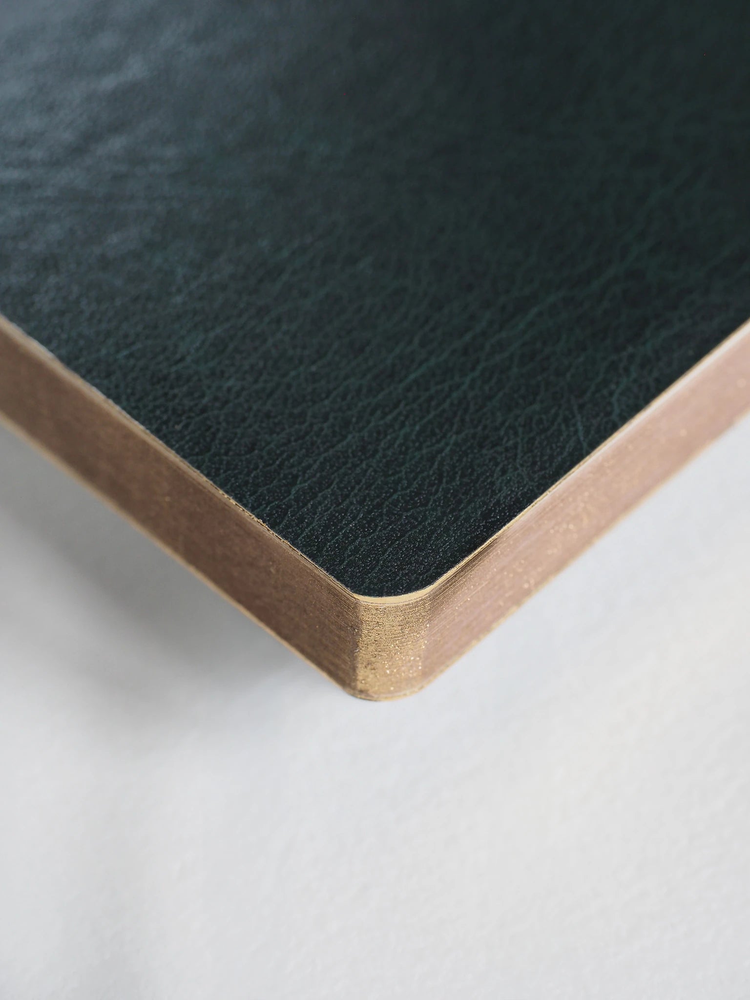 Close-up of a dark green textured leather corner with a light natural wood edge on a white surface.
#Color_Forest