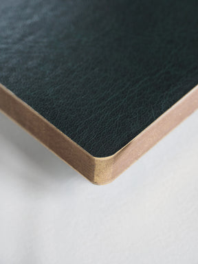 Close-up of a dark green textured leather corner with a light natural wood edge on a white surface.
#Color_Forest