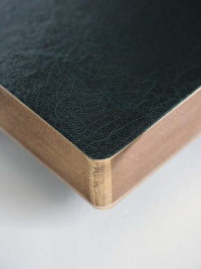 Close-up of a dark green textured leather corner with a natural wood edge on a light gray background.
#Color_Forest
