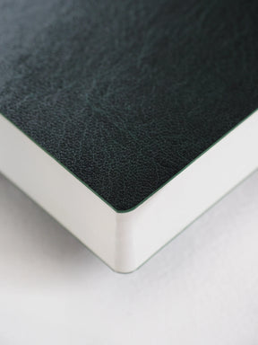 Close-up of a book or notebook corner showing a dark textured cover and a white page block on a light background.
#Color_Forest