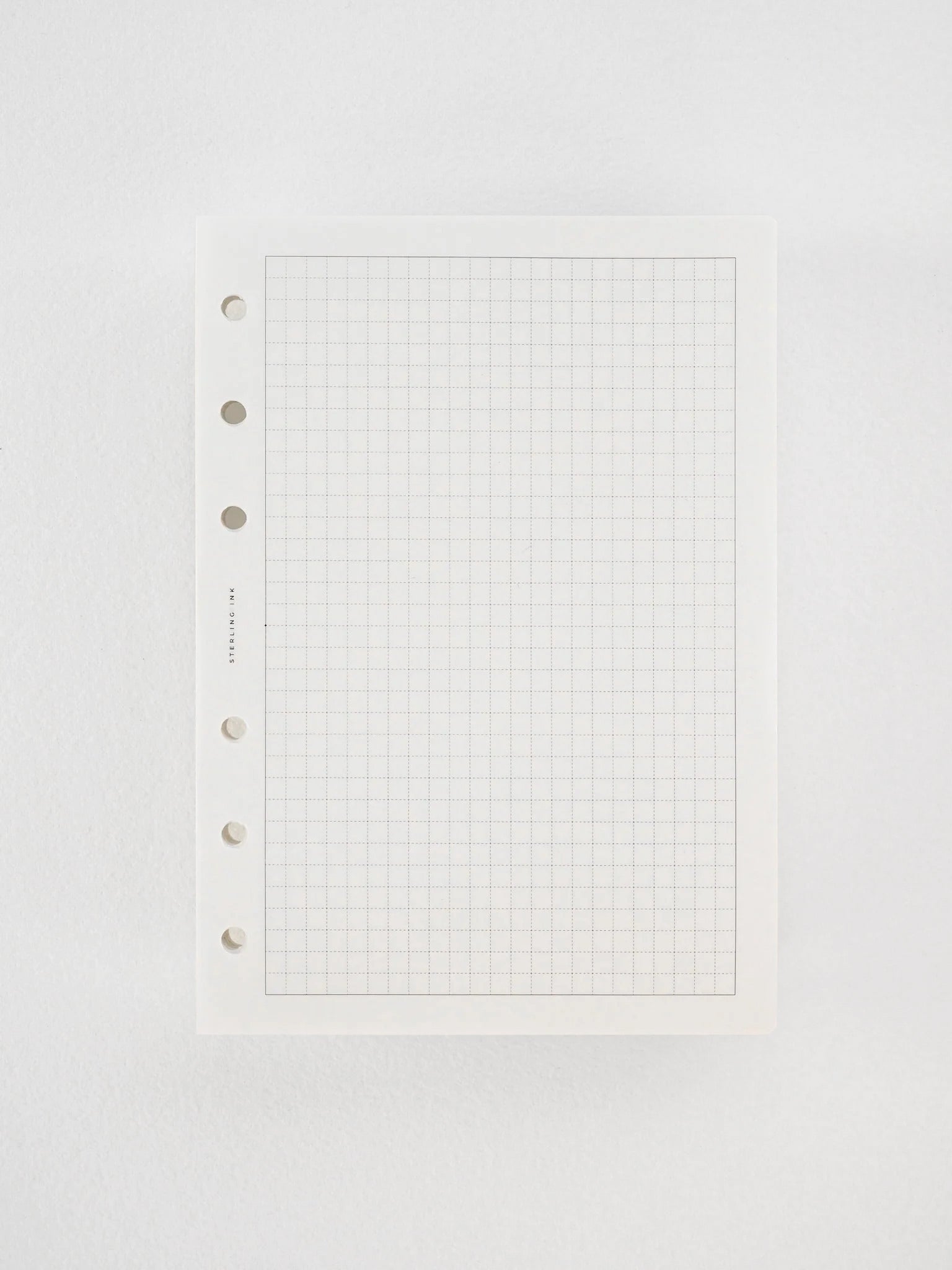 Pristine sheet of white graph paper featuring precise, light black grid lines for structured writing and three binder holes along the left edge.